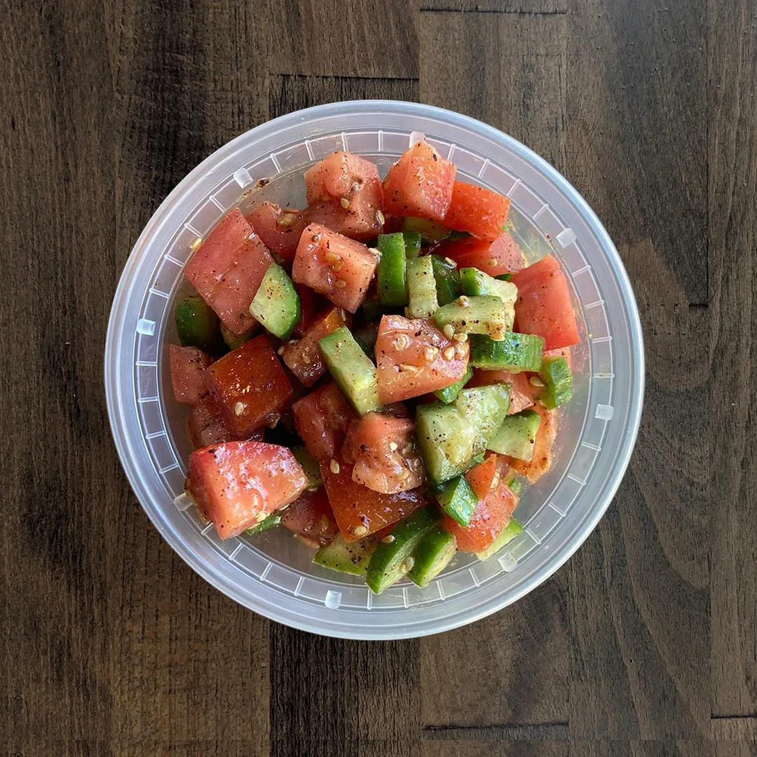 Brightly colored Cucumber Tomato Salad is in a circular container on a wood table background.