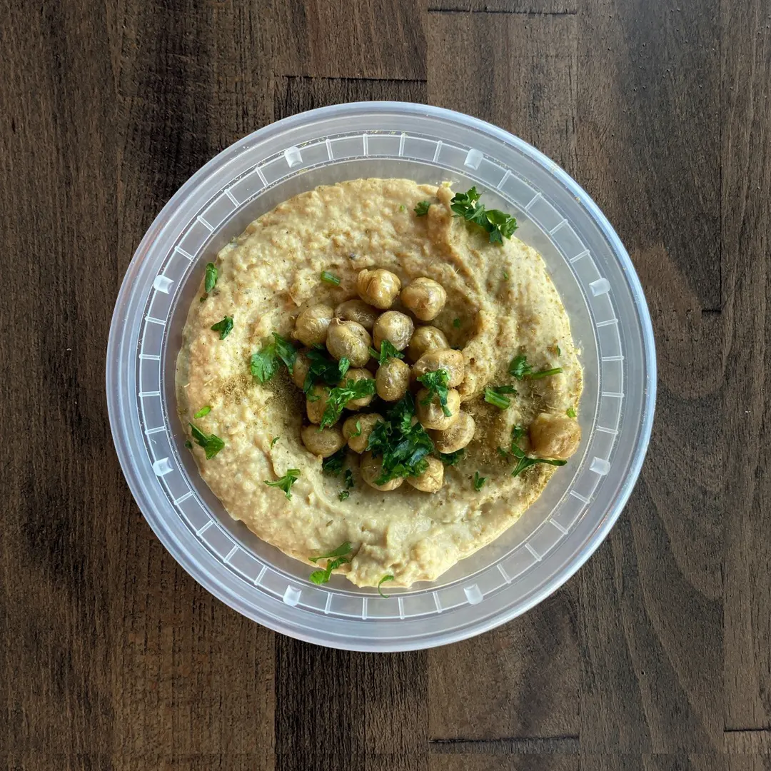 Silky smooth Curry Hummus is in a circular container topped with garbanzo beans and parsley on a wood table background.