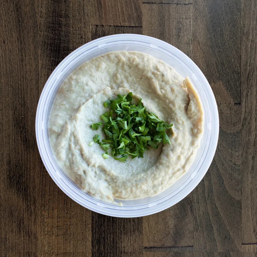 Baba Ghanoush is placed in a circular container on a wood table background. The Baba Ghanoush is topped with a parsley garnish.