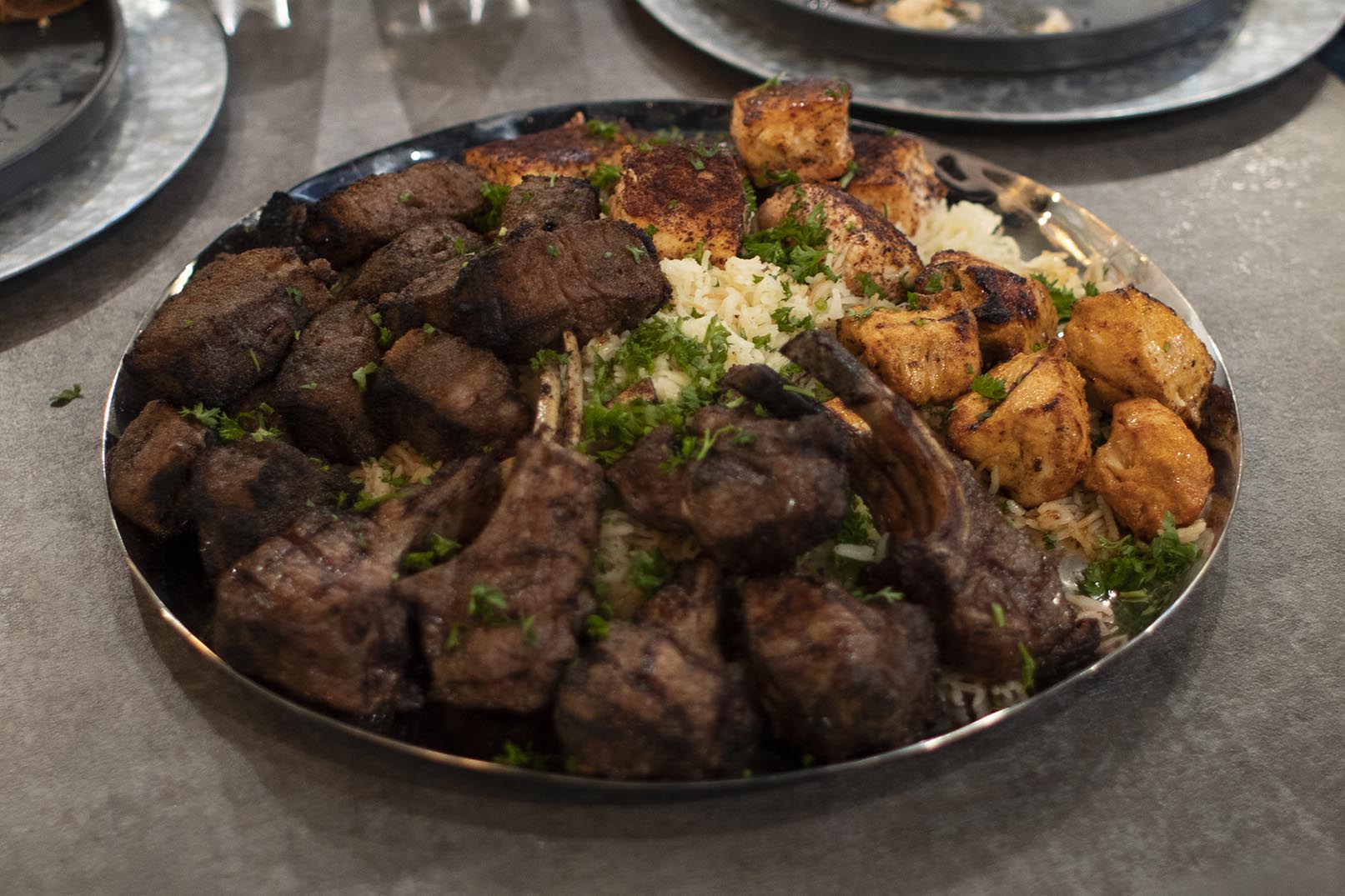 In the Hummus Labs restaurant the main course is placed out on a large round platter for the evening’s Chef’s Table. The platter is topped with A5 Wagu Beef Kabob, Grilled New Zealand Lamb Chops, Mediterranean Salmon, and Chicken Kabob served over a bed of rice.