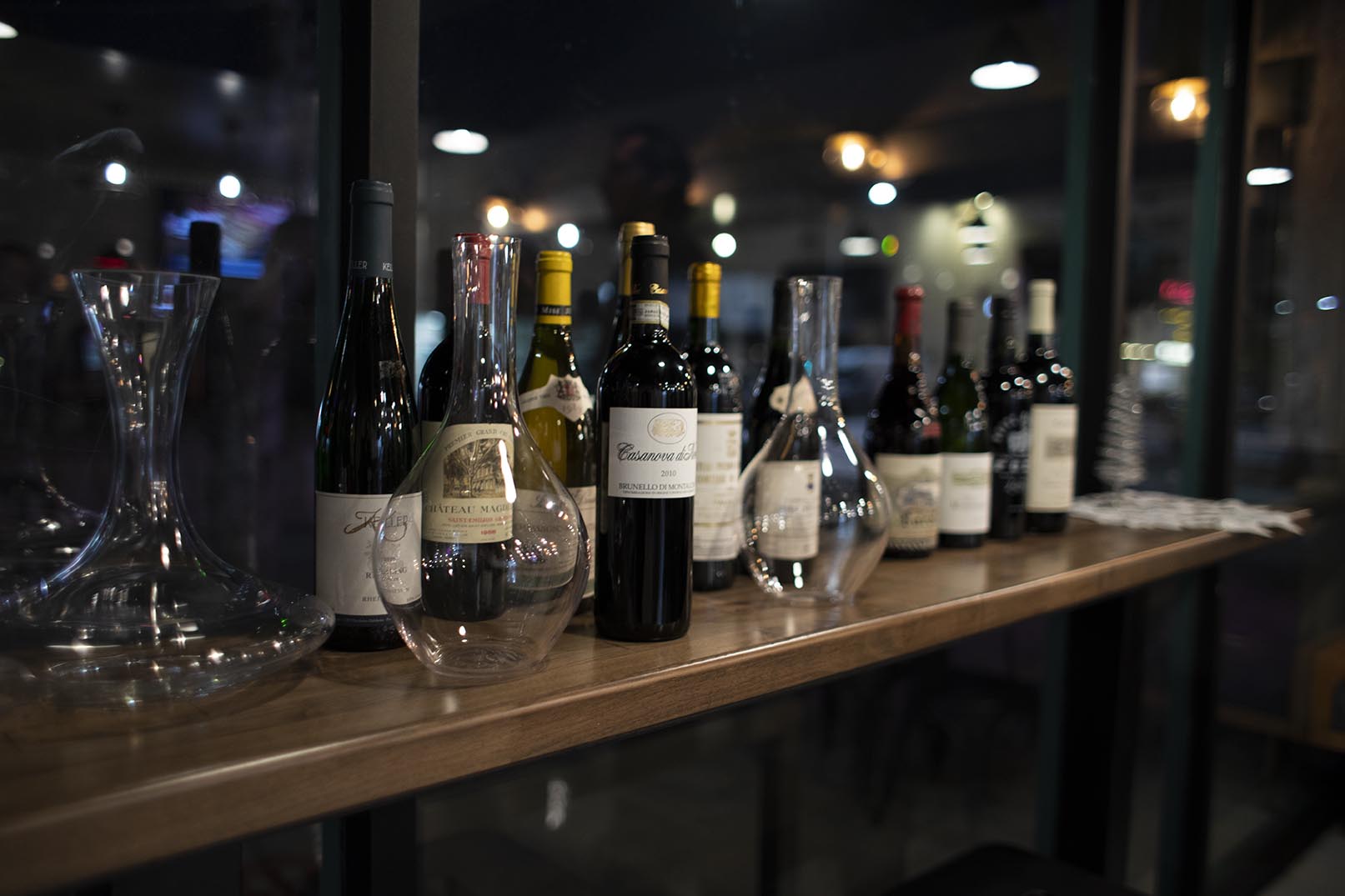 In the Hummus Labs restaurant on a wooden bar, a variety of vintage wines and glass carafes are placed. 